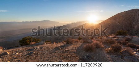 Sun rays over mountain range in desert. This is a panorama image taken of Keys View in Joshua Tree National Park in California at sunset. The last sun rays hover over the mountainous desert landscape.
