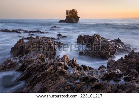 Rocky coastal sunset seascape with orange sky.  This is a long exposure image of rocky coastal sunset with orange sky in the background.