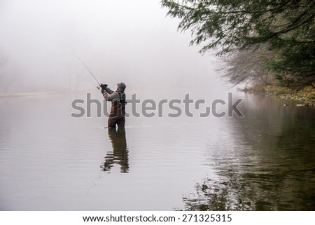 a man wearing waders casts his fishing pole in a river