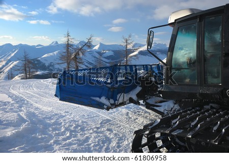 A part of black snowcat with cabin. Caterpillar track on the snow. Evening mountains background
