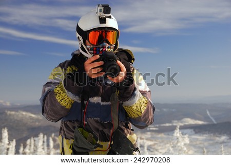 Snowboarder with action camera on helmet and SLR camera in his hands