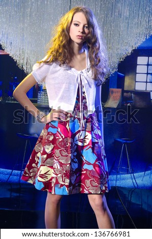 Young beautiful female model in colorful dress posing in bar