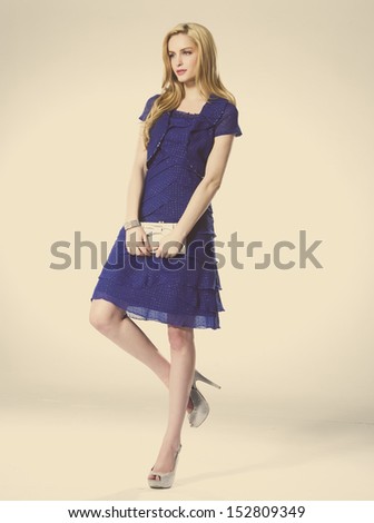Young beautiful blond girl holding purse posing on beige background