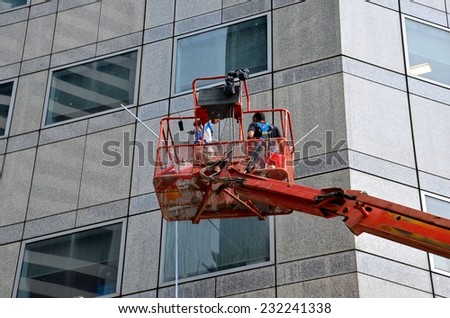 Singapore - April 25, 2013: A two man cleaning crew on a snorkel carrier with mops and other cleaning devices cleans the walls and windows of a tall building in Singapore\'s Raffles business district.