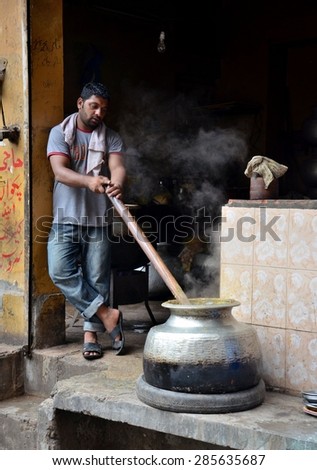 Lahore, Pakistan - September 9, 2012: A young man cooks / stirs a traditional Pakistani breakfast dish early inside Lahore\'s old walled city, near Bhatti Gate. Note the tire on which the pot sits.