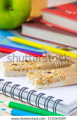 Healthy school lunch for child with stick berry muesli and green apple, books, notebooks and colorful pencils around
