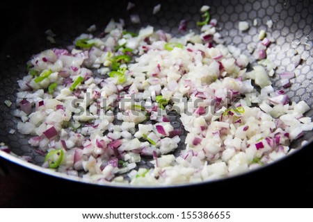 Sliced red and white onion passer in frying pan with garlic and green chilli