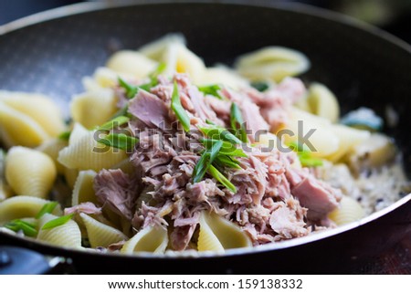 Pasta with tuna, zucchini, sauce and herbs in a frying pan, home cooking