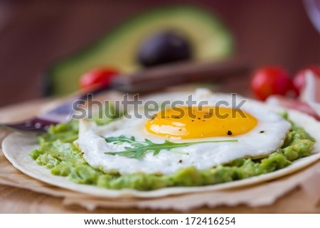 Breakfast with fried egg and sauce of avocado on grilled flour tortilla, Mexican dish huevos rancheros