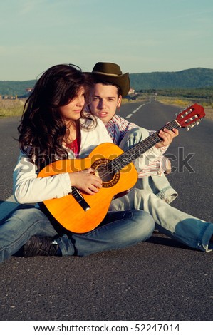 Young Couple Sitting in Middle of Road with Guitar