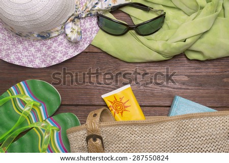 beach accessories on wooden board (straw hat, scarf, sunglasses, beach bag, sunblock, book, flip flops)