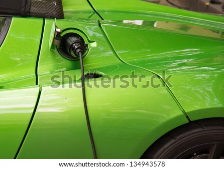 Green electric car charging: Close-up of indistinguishable electric car \'fueling\', i.e. plugged to the electricity hose, charging battery.