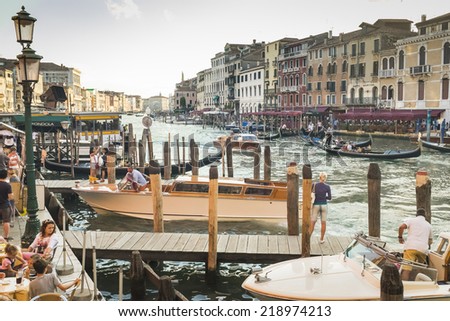 VENICE, ITALY - AUGUST 15, 2014: late afternoon urban scene, in the busy canal by the Rialto bridge. A main global tourist attraction, Venice annually receives ten times its population in visitors