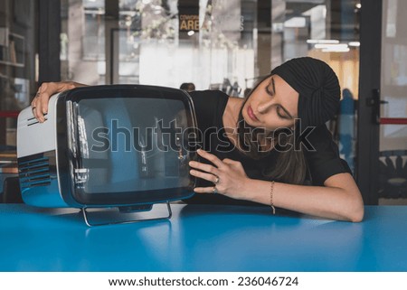 Beautiful young brunette with turban posing beside a vintage tv