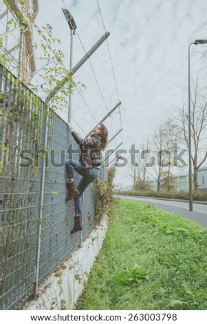 Beautiful young brunette with long hair climbing over a fence