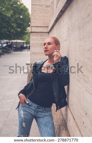 Beautiful blonde girl wearing ripped jeans and leather jacket smoking a cigarette in the city streets