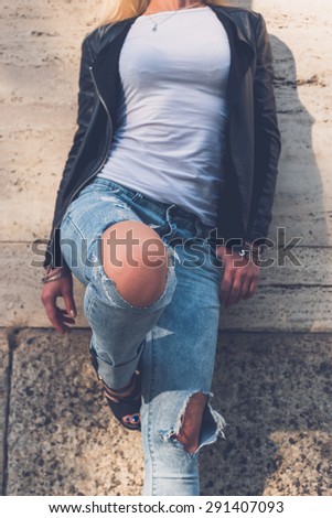 Detail of a beautiful girl wearing ripped jeans and leather jacket posing in the city streets