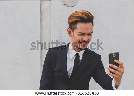 Young handsome Asian model dressed in dark suit and tie taking a selfie