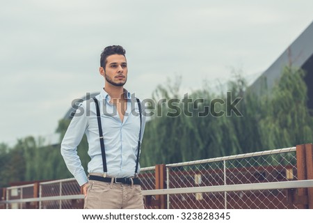Young handsome man with short hair and beard wearing suspenders and posing in an urban context