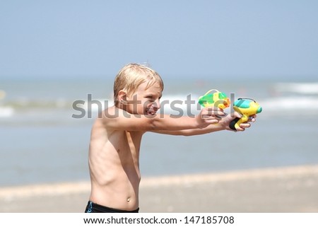 Cute boy playing with water guns on a beautiful beach at the sea