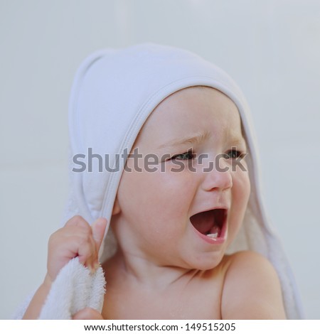 Lovely angry cute baby girl under bath towel is screaming loud from emotions