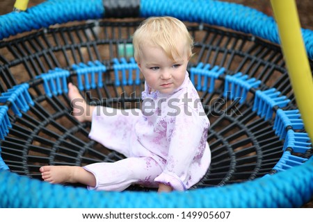 Funny baby girl in a beautiful kimono suit plays on a rubber net swing at a playground in the park