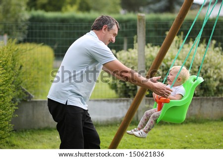 Happy father with his cute baby daughter playing with swing in the garden at backyard of the house
