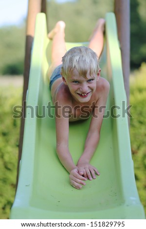 Happy seven years old boy playing outdoors in playground going down on a slide