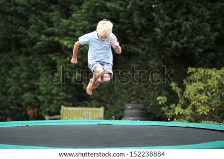 Happy teenager boy plays outdoors in garden jumping high in the sky on trampoline