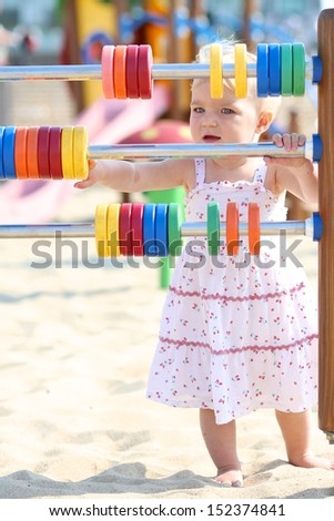 Adorable blond baby girl plays outdoor at the beach sandy playground learning to count with bright rainbow colored rings
