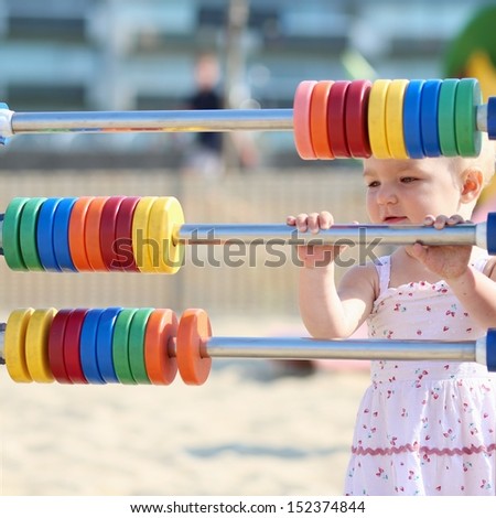 Cute blond baby girl plays outdoor at the beach sandy playground learning to count with bright rainbow colored rings
