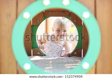 Cute smiling blond baby girl plays peek a boo at playground