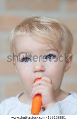 Lovely little blond baby girl bites on delicious fresh raw carrot