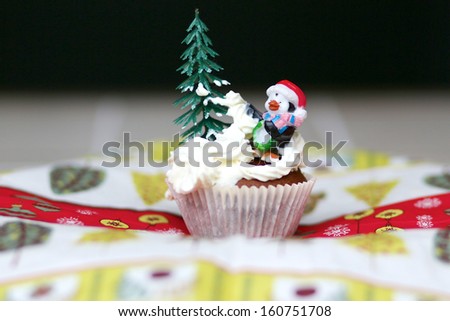 Funny christmas cake, a cupcake decorated with xmas tree and penguin in red hat placed in the whipped cream snow