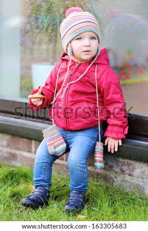 Cute little toddler girl plays outdoors sitting outside of the house next to the big front window