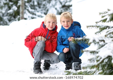 Two boys, twin brothers, in colorful warm coats playing outdoors in the snow