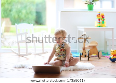 Cute blonde little toddler girl playing with notebook indoors at home or kindergarten