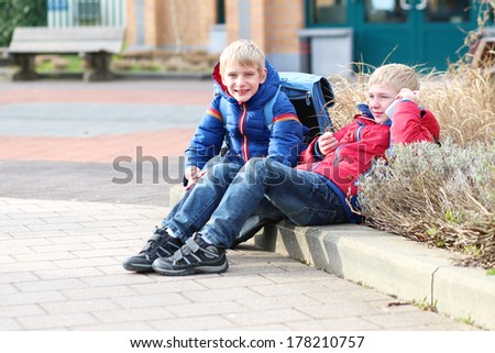 Teenager boys twin brothers calling on mobile phone sitting outside of the school