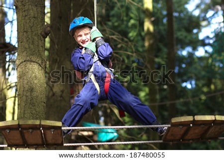 Happy healthy teenager school boy enjoying activity in a climbing adventure park on a sunny summer day