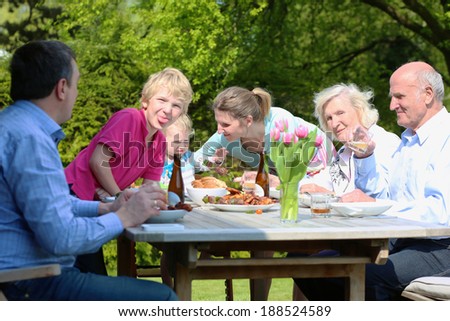 Big happy family with kids and grandparents having healthy tasty bbq lunch or dinner outdoors in the garden at the backyard of their house eating grilled meat with vegetables on a sunny summer day