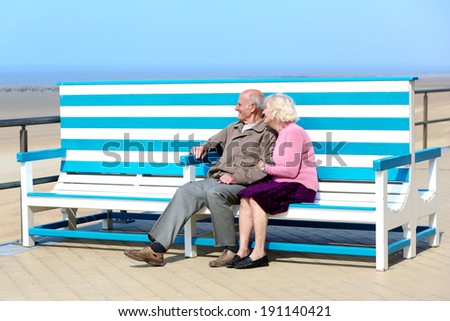 Happy senior couple relaxing on the beach sitting together on the bench - active retirement concept