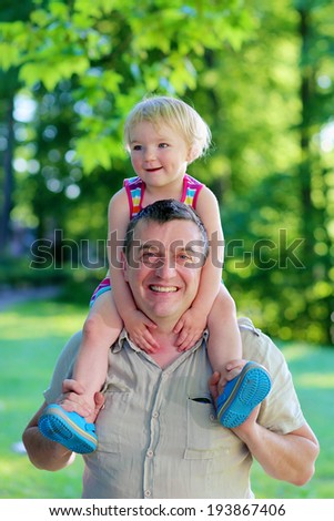 Happy family, a father and his daughter, cute toddler girl with blonde curly hair, enjoying time outdoors, hugging and kissing, on a sunny summer day