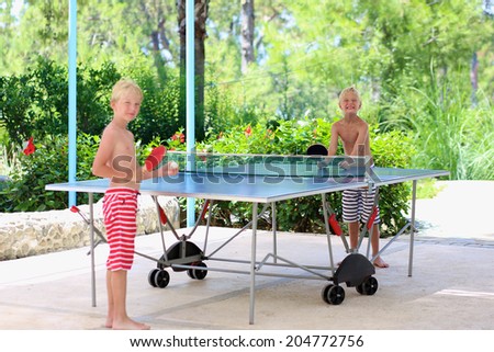 Two happy boys, teenager twin brothers, enjoying summer vacation playing ping pong outdoors