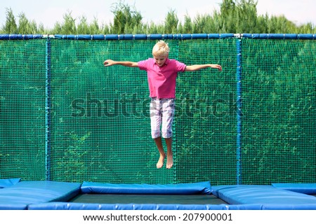 Happy child, active teenage school boy plays outdoors in playground jumping high in the sky on trampoline