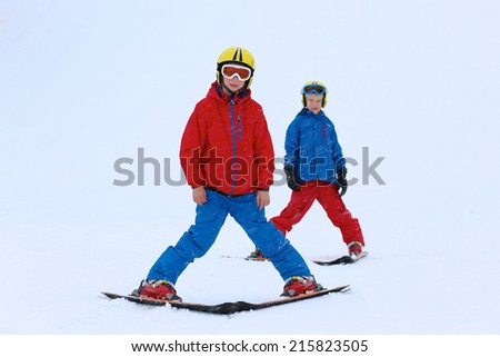Two happy school  boys, twin brothers in colorful snowsuits, having fun skiing in alpine mountains during snowy winter vacation