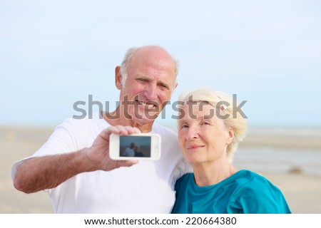 Happy loving senior couple enjoying vacation together having fun on the beach taking selfie photo using smartphone camera. Concept of active retirement and interaction with new technologies and trends