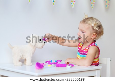 Little child, adorable blonde toddler girl, playing doctor role game and treating her puppy using her imagination and different medical tools