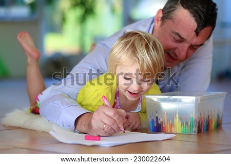 Happy family of two, loving caring father with child, adorable toddler girl, spending time together at home lying cozy on tiles floor on warm lambskin drawing picture with colorful felt-tip pencils