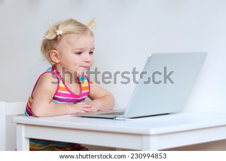 Happy little child, blonde toddler girl, playing with laptop at home or school - early development and education concept