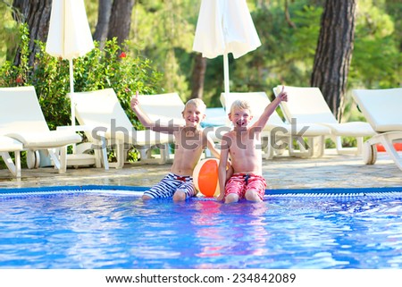 Two happy boys, laughing teenage twin brother, enjoying sunny summer vacations playing with inflatable ball in outdoors swimming pool
